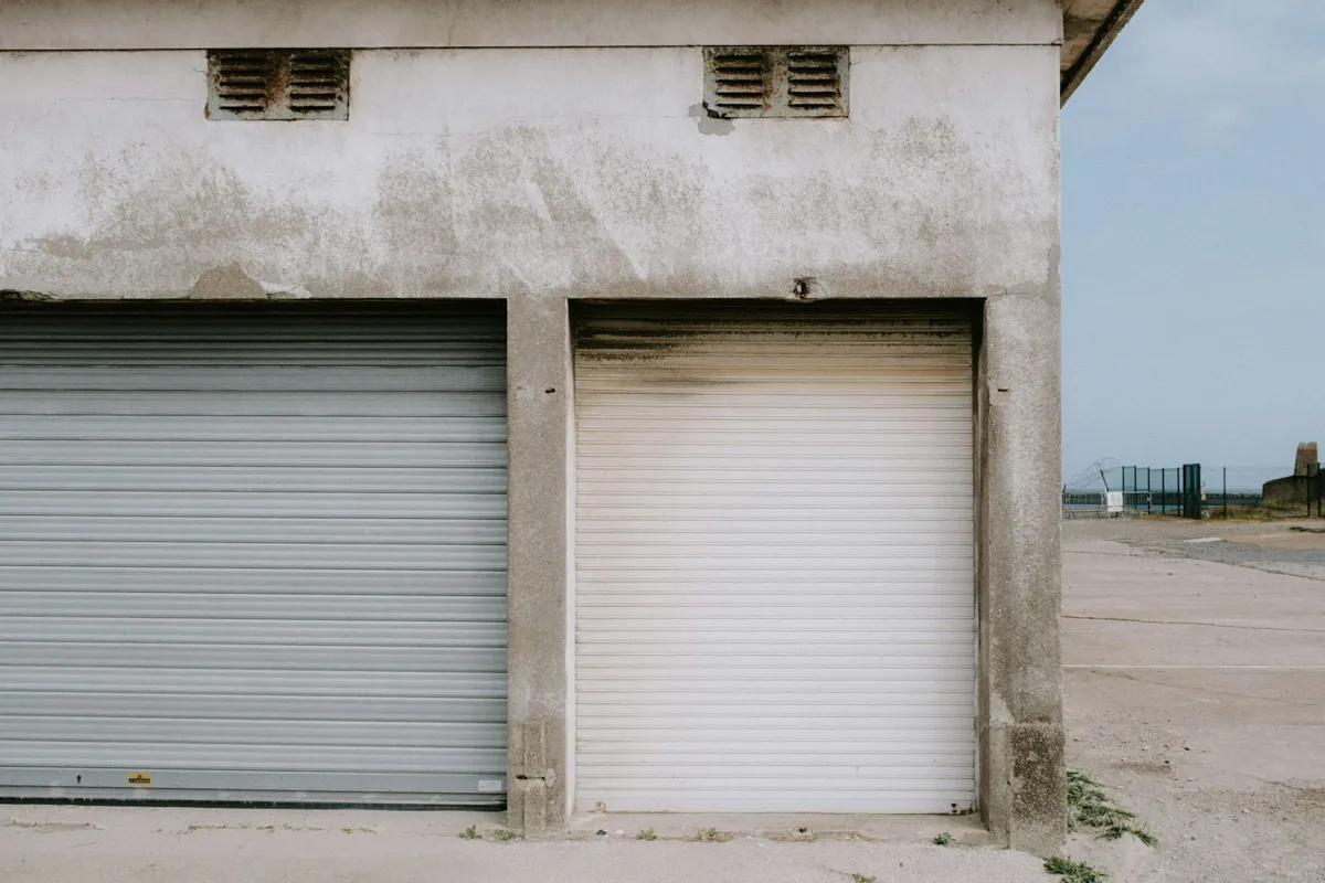 Two roll-up doors, one gray and one white, in a concrete building