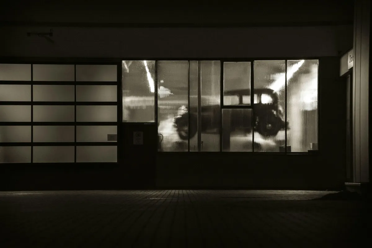 Glass garage door at night with a classic car visible inside