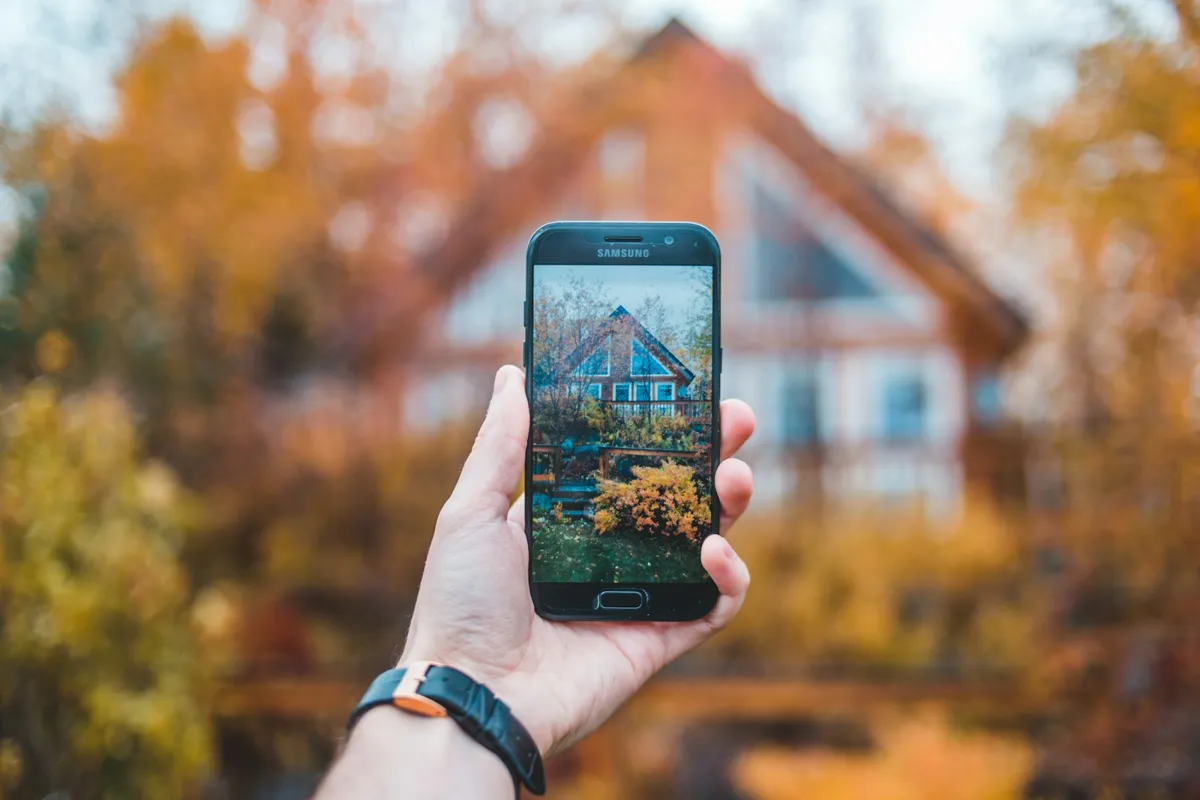 Hand holding a phone with a house in the background